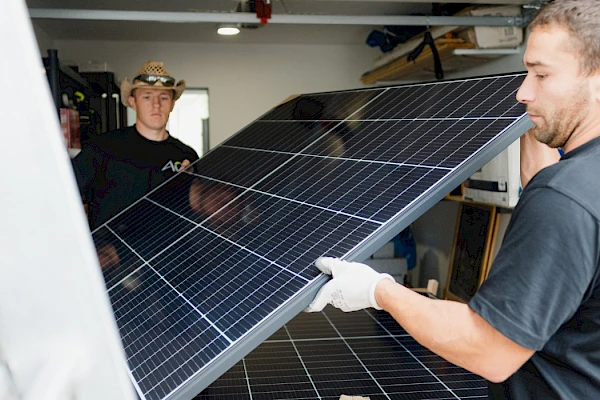 Zwei Arbeiter transportieren eine Solarplatte.