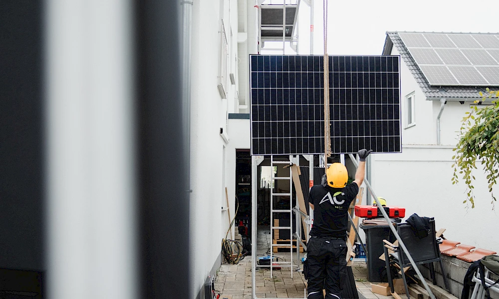 Ein Solarmodul wird mit einem Seilzug an einer Hauswand nach oben transportiert.