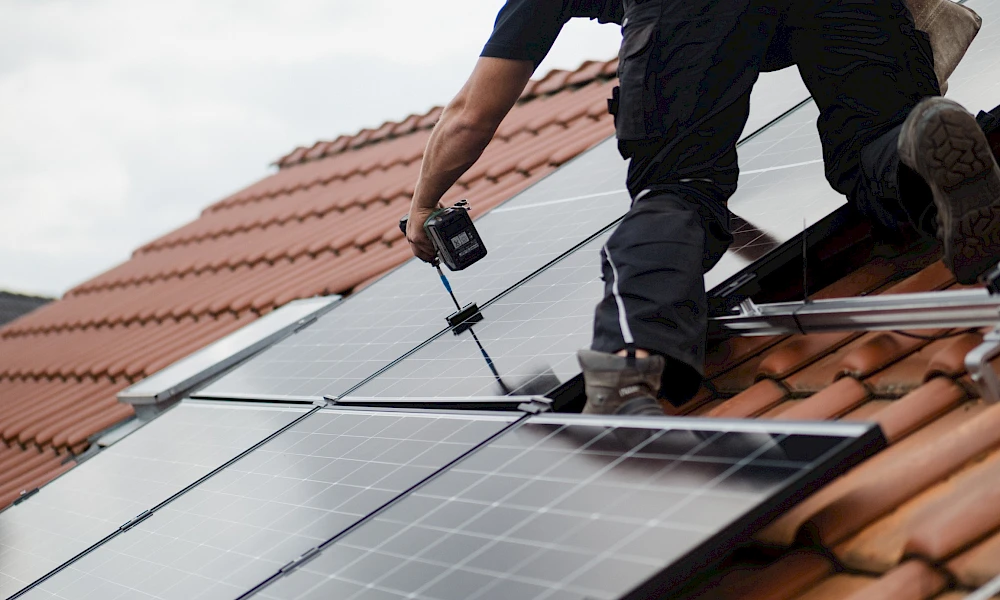 Nahaufnahme eines Handwerkers beim Ausrichten und Befestigen eines schwarzen Solarmoduls.